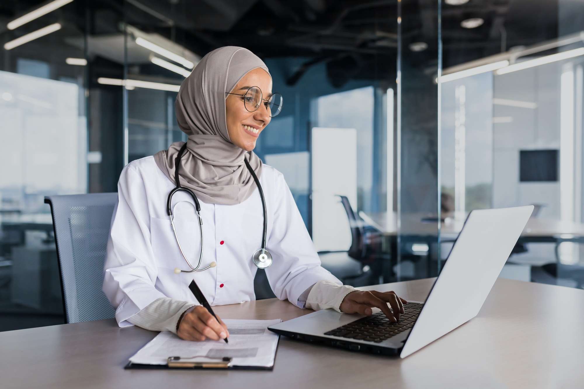 Arab muslim woman in hijab doctor working in modern clinic office with laptop, doctor on paper work